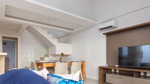A modern hotel room with a dining area, a large flat-screen TV, and an air conditioning unit.