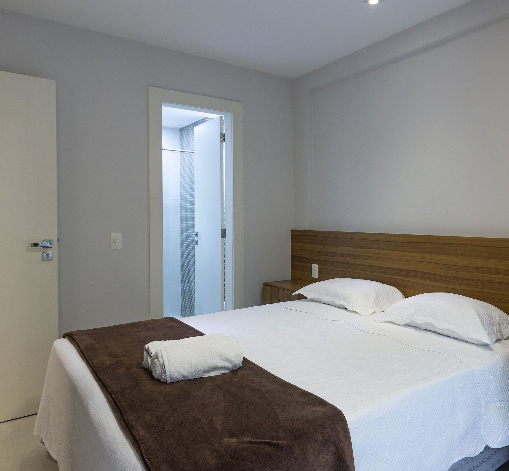 A neatly made bed with a brown blanket and white pillows, a wooden headboard, and a white door with a window.