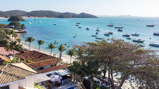A coastal hotel with a beach view, multiple boats in the water, and palm trees.