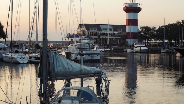 Ein Yachthafen mit mehreren Segelbooten, ein Leuchtturm und ein Gebäude mit einem Balkon mit Blick auf das Wasser.