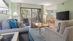 Ein Wohnzimmer mit einer Couch, einem Couchtisch, einem Fernseher und einem Essbereich mit Stühlen und einem Tisch.