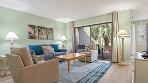 Ein Wohnzimmer mit einer Couch, einem Sessel, einem Couchtisch und Blick ins Freie.