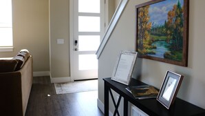 A hallway with a brown couch, a door, a staircase, and a painting of a landscape. - New 3BR w/ Garage, 1 Mile from Downtown (Hamilton)