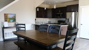 A modern kitchen with dark wooden cabinets, stainless steel appliances, and a dining area with a wooden table and chairs. - New 3BR w/ Garage, 1 Mile from Downtown (Hamilton)