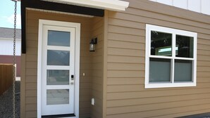 A house with a beige exterior, a white front door with a glass panel, and a small window to the right. - New 3BR w/ Garage, 1 Mile from Downtown (Hamilton)