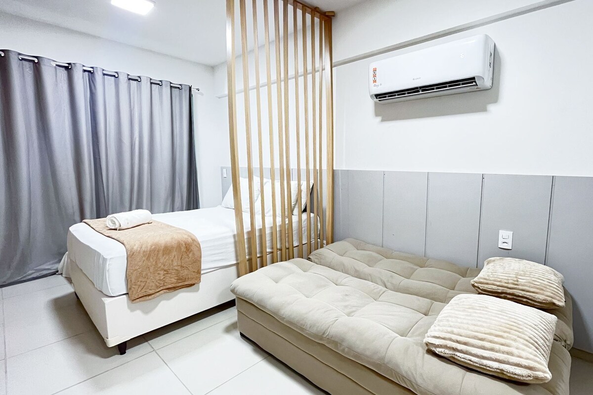 Una habitación con una cama, un sofá, una cortina, un ventanal y un equipo de aire acondicionado.