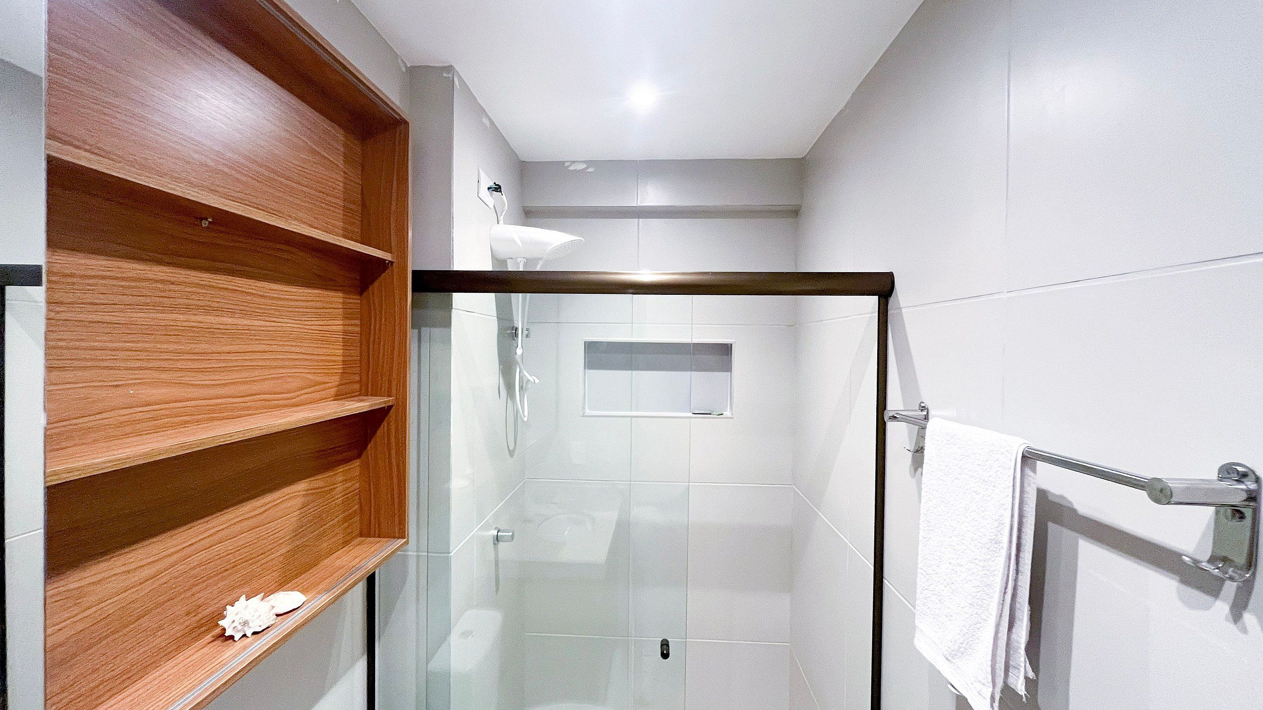 A modern bathroom with a glass shower enclosure, a wooden shelf, and a towel rack.