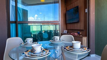Una mesa con cubierta de vidrio, rodeada de sillas, con vista al exterior a través de un ventanal.