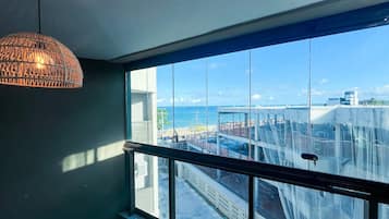 Quarto com janelas amplas, luminária pendente e vista para o mar e um edifício.