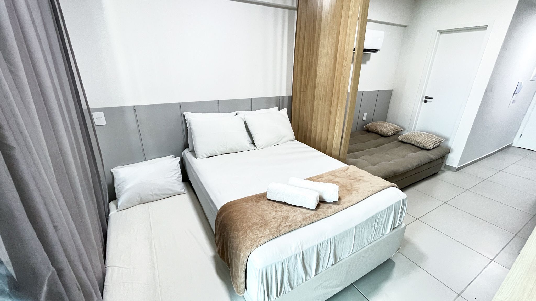 A hotel room with a bed, a sofa bed, a wooden column, and a door.