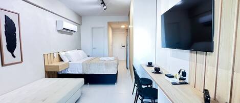 Una habitació d'hotel moderna amb un llit, un sofà, un televisor fixat a la paret i una taula petita amb cadires.
