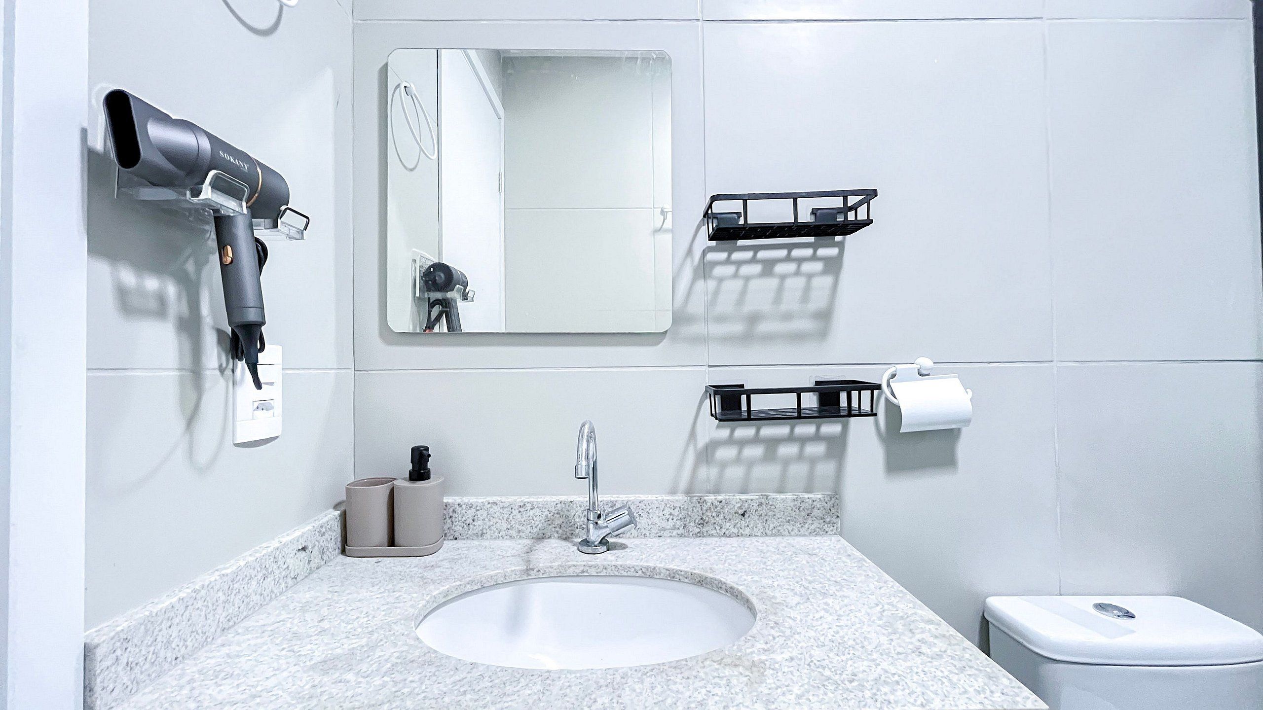 A bathroom with a sink, mirror, towel rack, toilet, and a hairdryer.