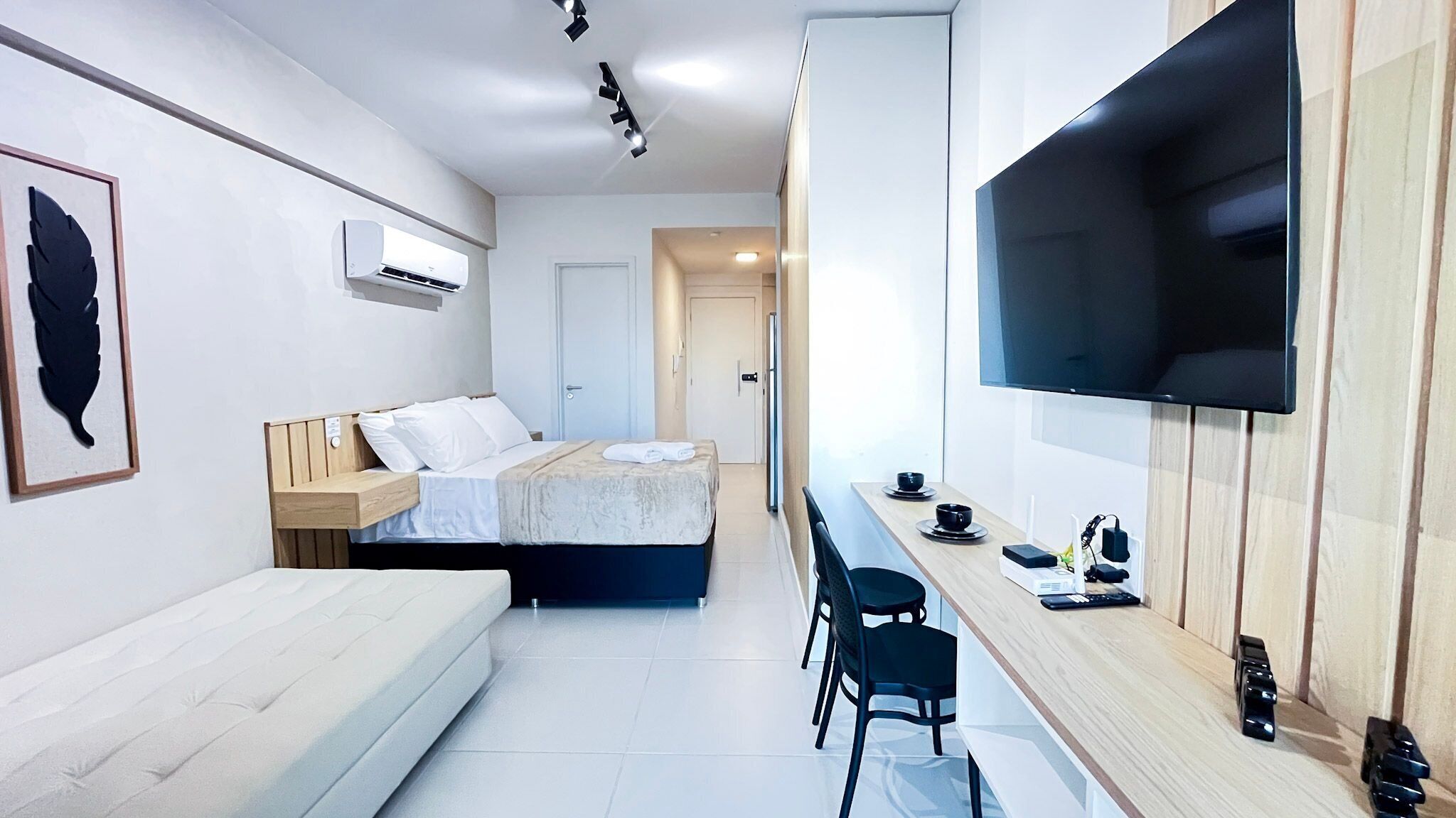 A modern hotel room with a bed, a sofa, a TV mounted on the wall, and a small table with chairs.