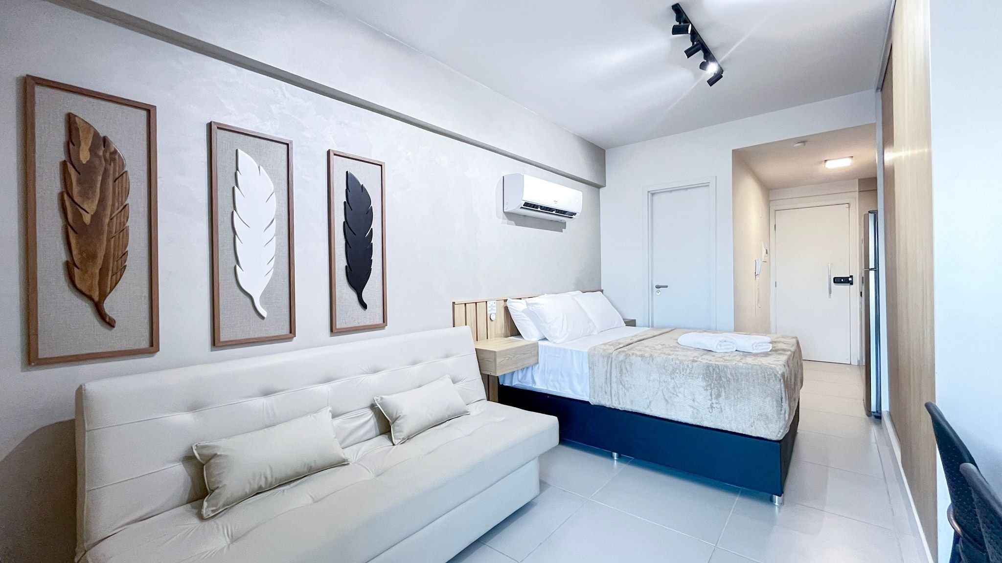 Une chambre à coucher comprenant un lit, un canapé et trois œuvres d’art représentant des feuilles, encadrées et accrochées au mur.
