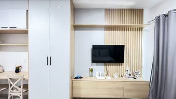 A modern room with a TV mounted on a wooden panel wall, a desk with a chair, and a cabinet with drawers.