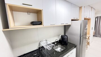 Una cocina compacta con estufa a gas, cafetera, escurreplatos y refrigerador.