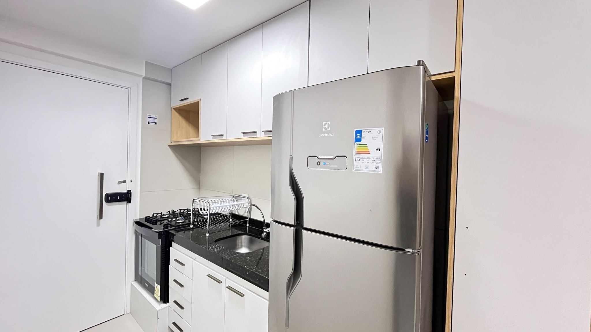 Una cocina compacta con refrigerador de acero inoxidable, estufa a gas y armarios blancos.