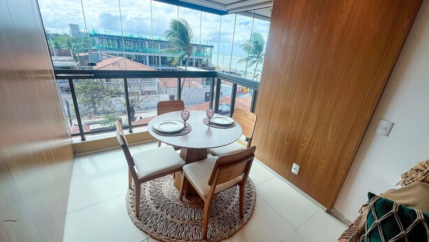 Un balcón con una mesa redonda y sillas, vista panorámica de la ciudad y una puerta de madera.