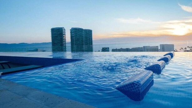 Une piscine à débordement offrant une vue sur deux bâtiments modernes et un coucher de soleil.