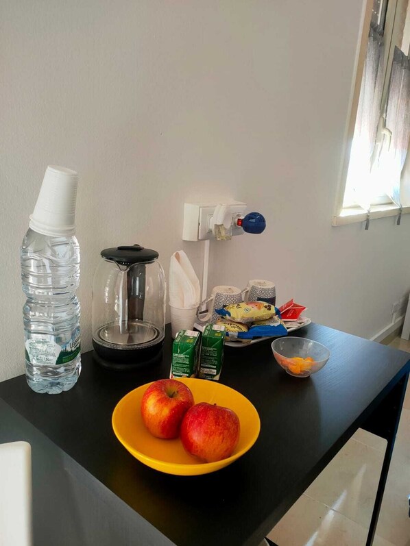 Eine Küchenarbeitsfläche mit einer Wasserflasche, einer Kaffeemaschine, einer Schüssel Äpfel und verschiedenen Lebensmitteln.
