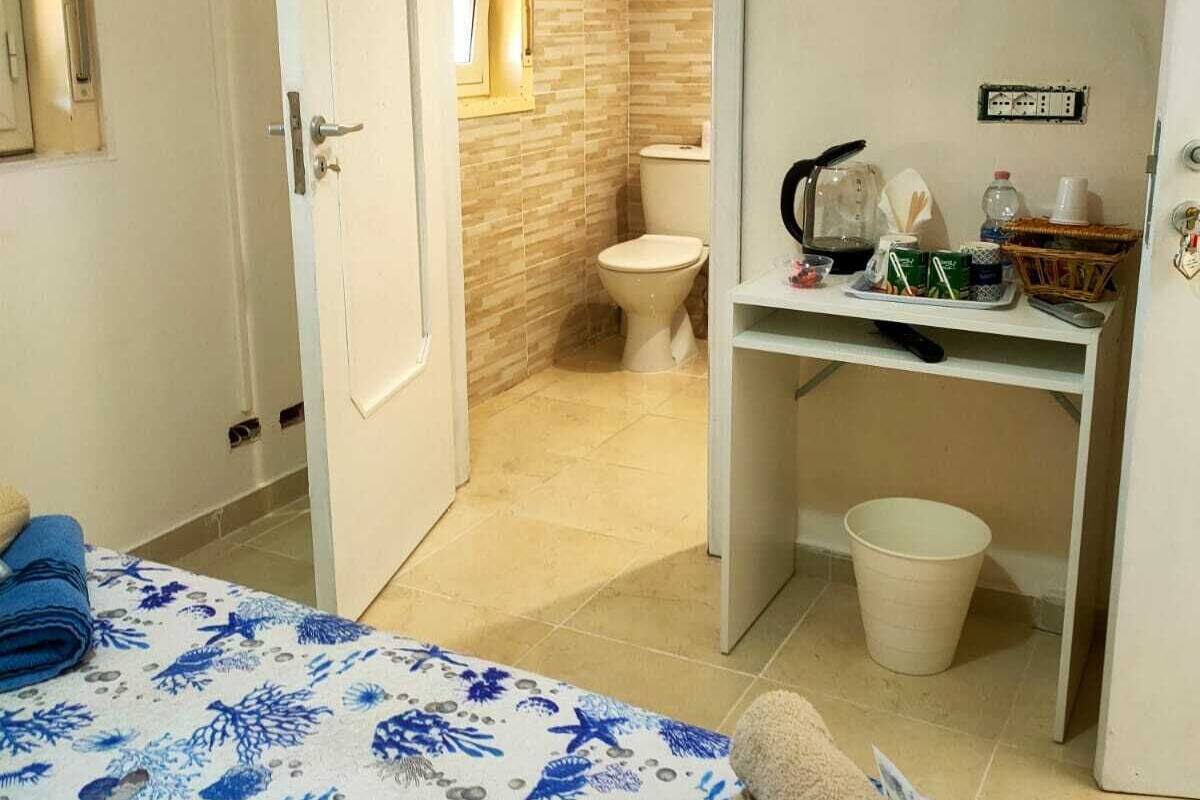 Habitación de hotel con cama, escritorio, televisor y baño visible a través de una puerta abierta.