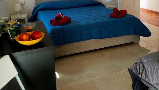 Un dormitorio con una cama, una mesita de noche con lámpara, un frutero y una puerta.