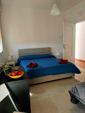 Un dormitorio con una cama, una mesita de noche con lámpara, un frutero y una puerta.