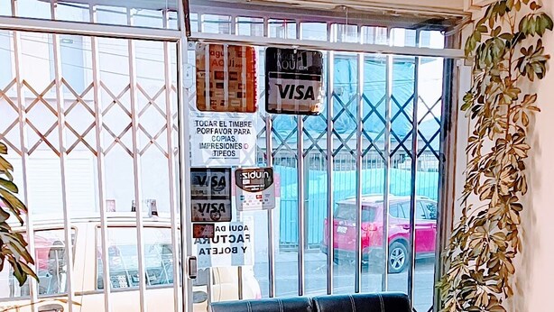 Eine kleine Sitzecke mit einer Bank, einem 'SALIDA'-Schild über der Tür und verschiedenen Zahlungsart-Kennzeichen, darunter VISA.