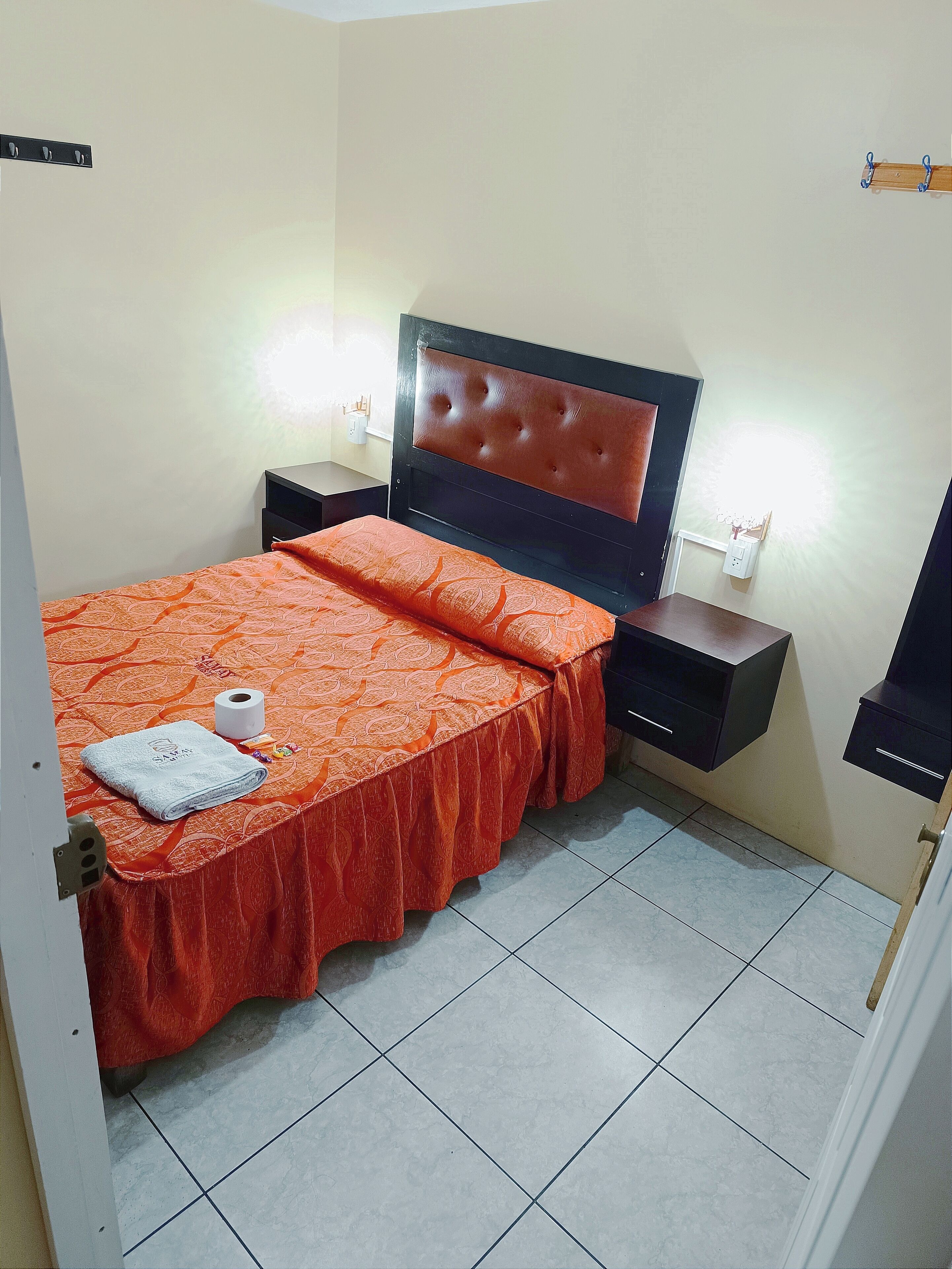 A bedroom with a bed, a nightstand, a wall-mounted TV, and a light fixture.