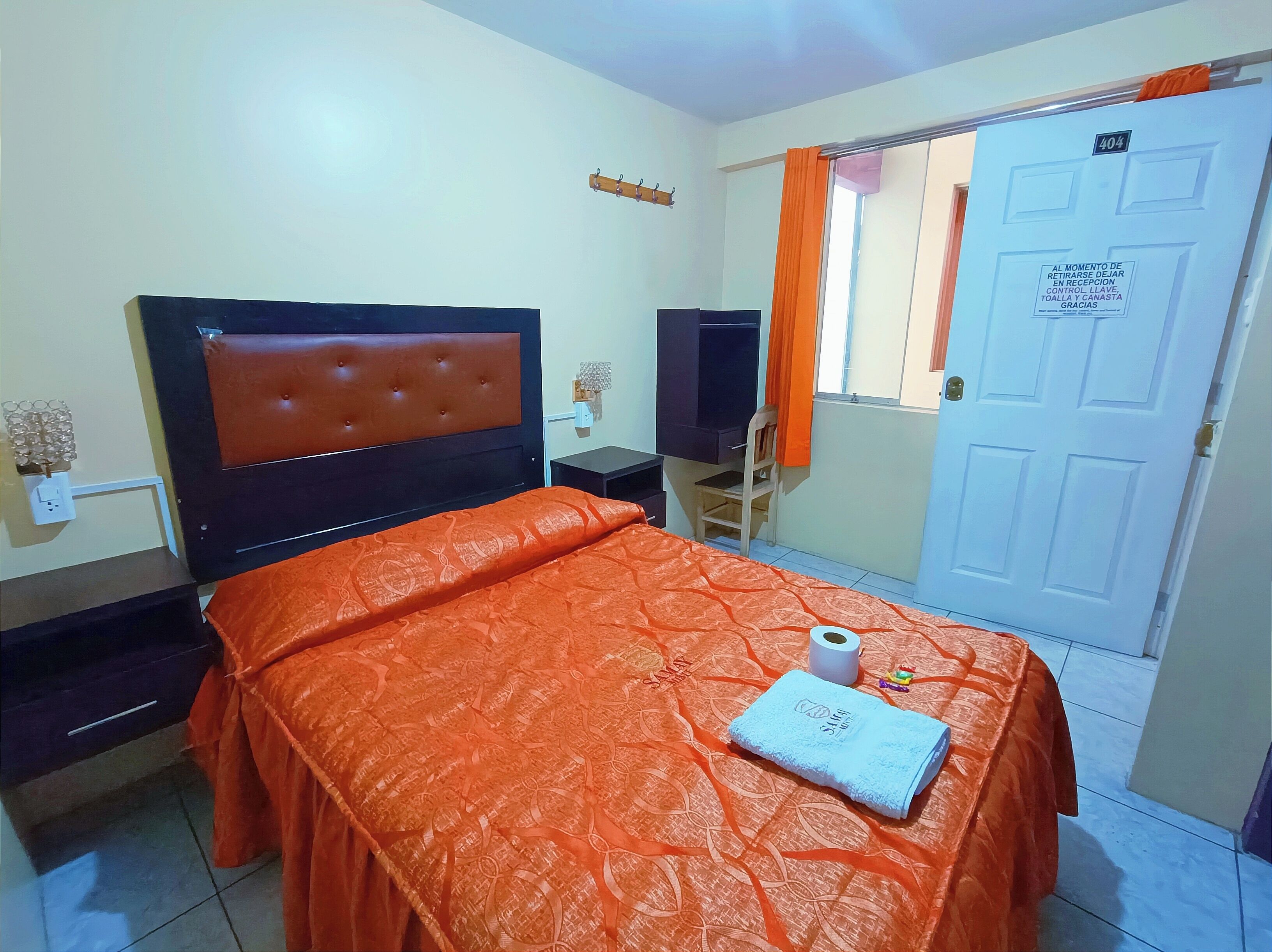 Une chambre d’hôtel avec un lit, un bureau, une chaise, une télévision et une porte avec une pancarte.