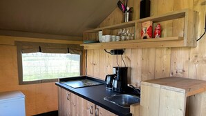Cocina compacta con armarios de madera, encimera negra, cafetera y ventana con vistas a la vegetación.