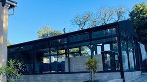 Un edificio moderno con grandes ventanales, un área de entrada pavimentada y plantas en macetas.