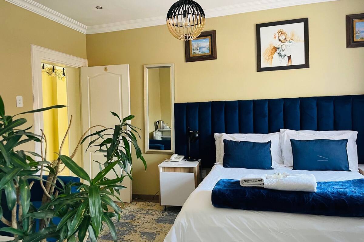 Una habitación de hotel con una cama grande, una mesita de noche, un espejo y una lámpara colgante.