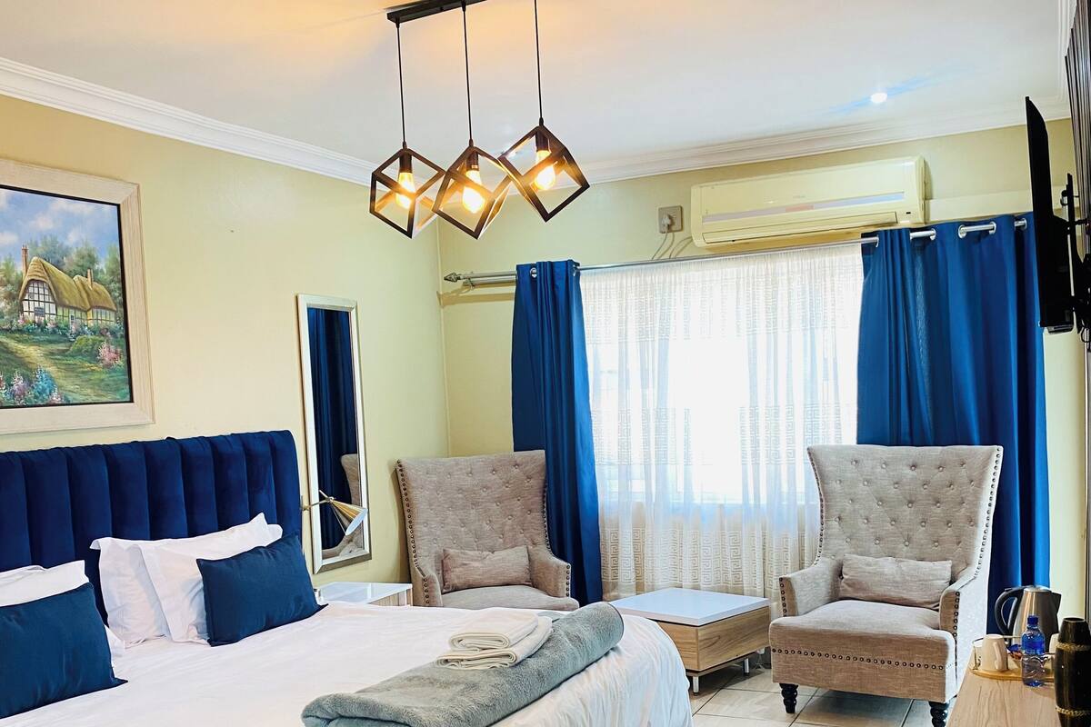 Habitación de hotel con una cama grande, dos sillones, una mesita de madera y un cuadro en la pared.