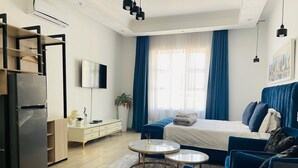 Una habitación de hotel moderna con cama, sofá, una mesita, televisión y refrigerador.