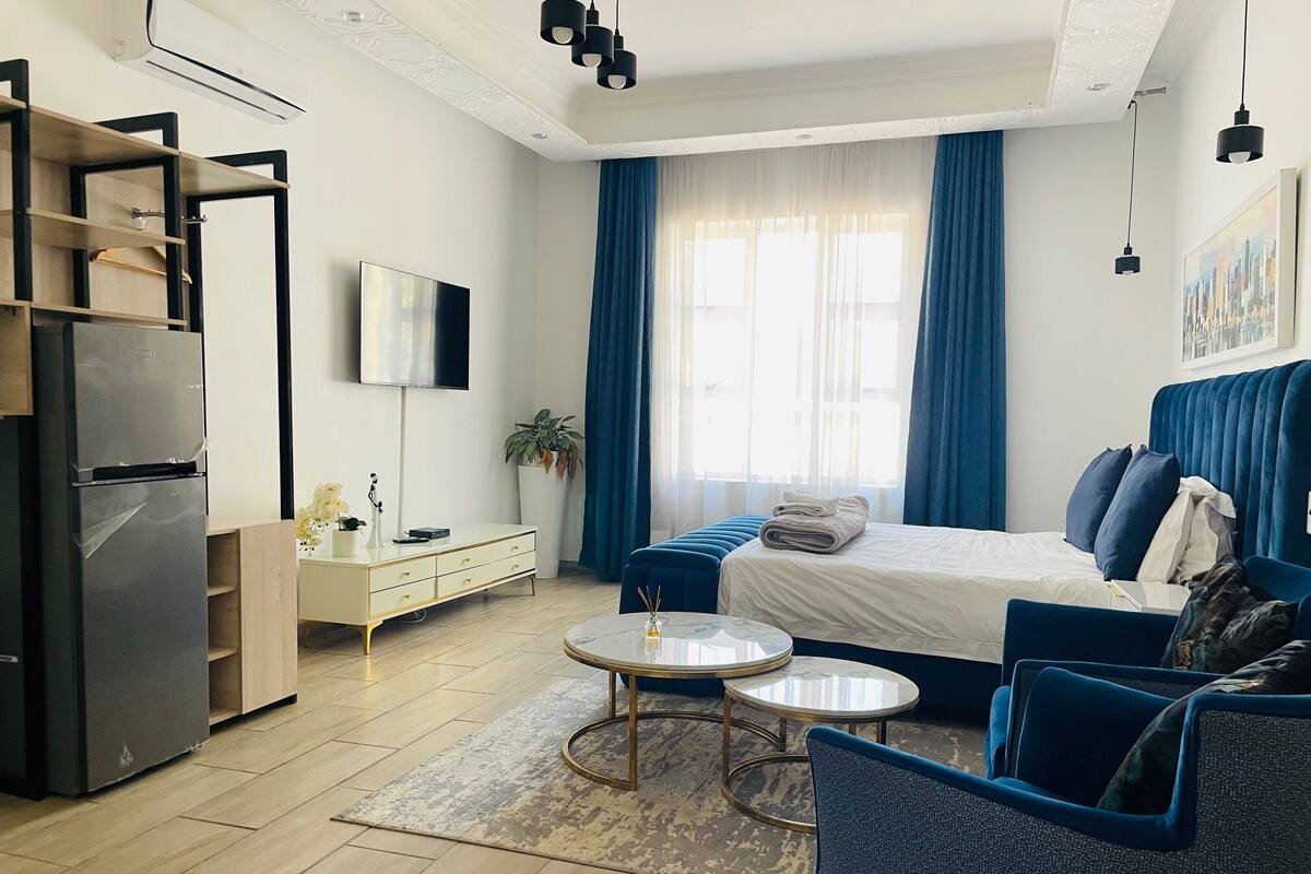 Una habitación de hotel moderna con cama, sofá, una mesita, televisión y refrigerador.