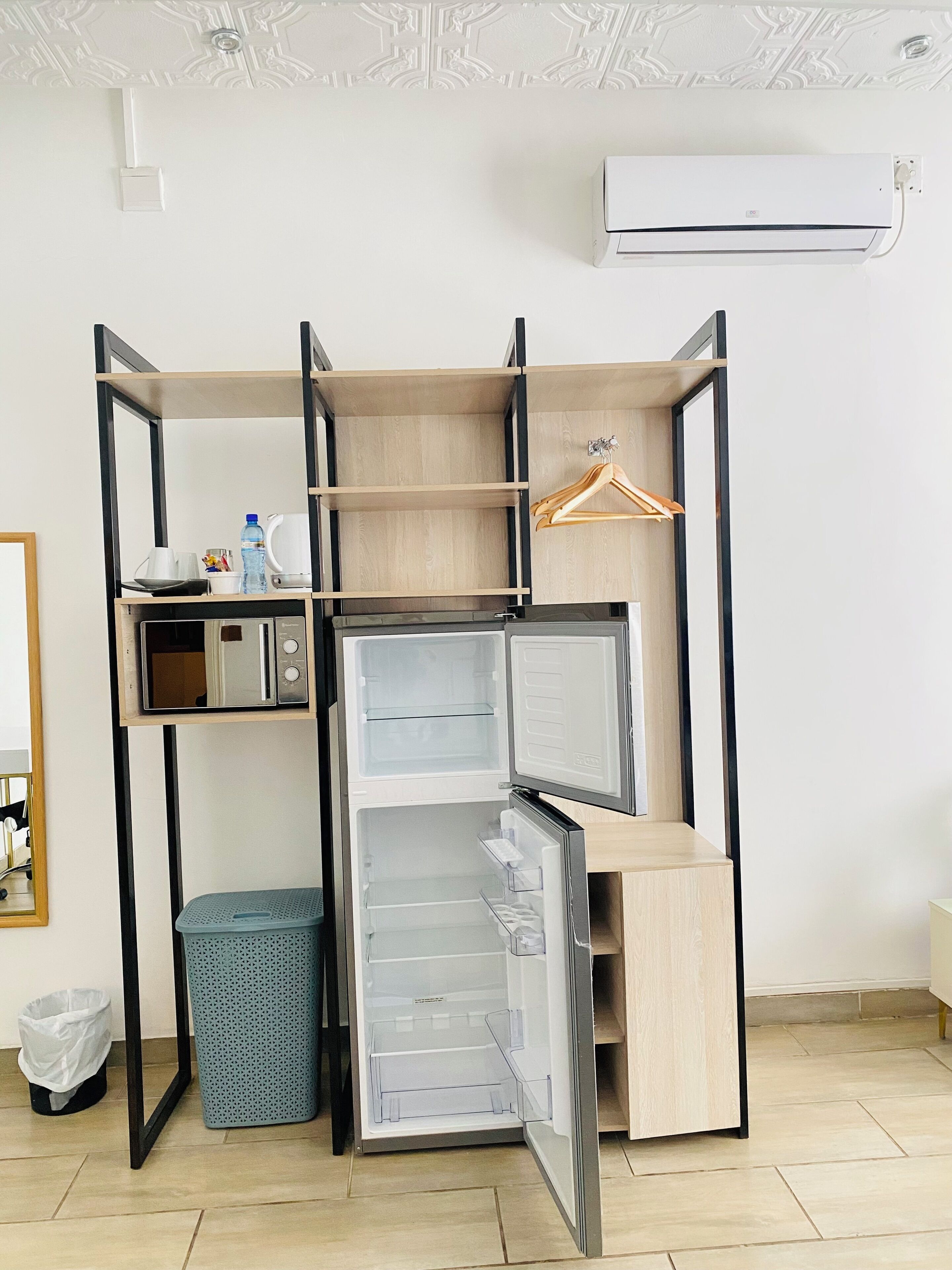Una kitchenette compacta con microondas, un perchero de madera colgante y un pequeño cubo de basura.