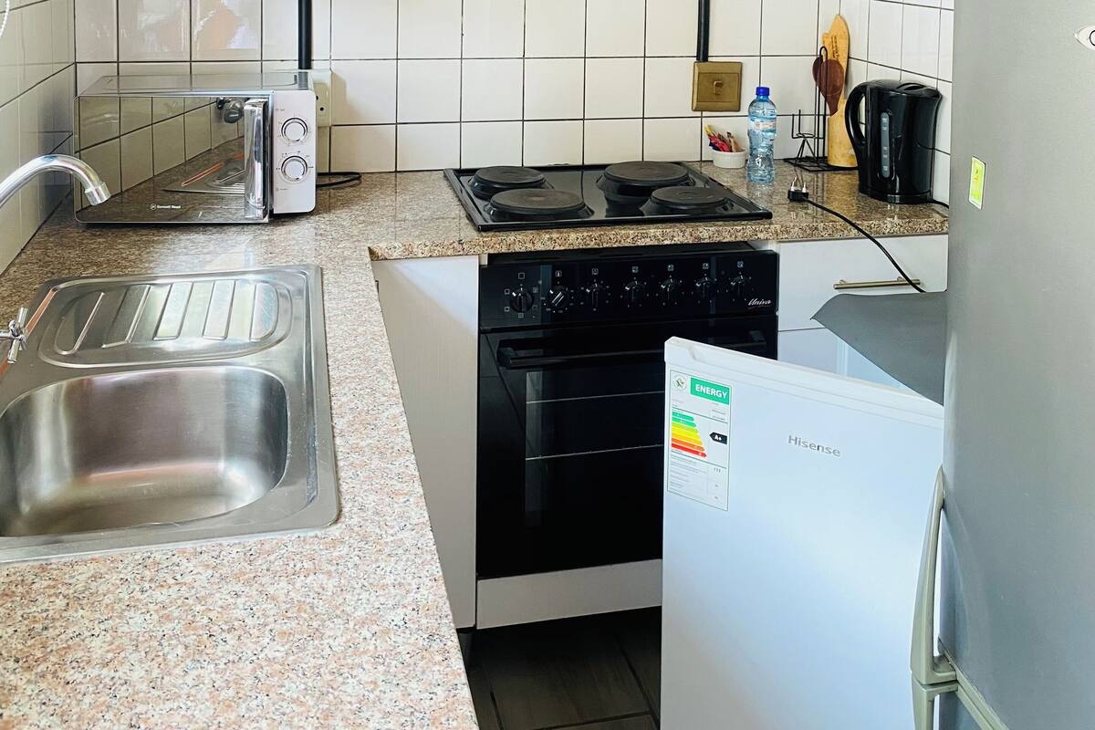 Una cocina compacta con armarios blancos, un lavamanos de acero inoxidable, un tostador, una estufa y un refrigerador.