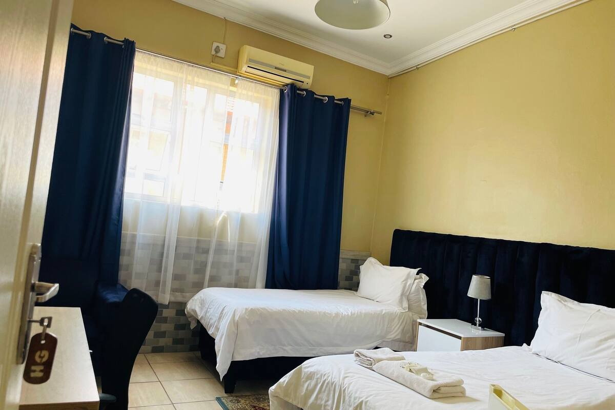 Una habitación de hotel con dos camas, un escritorio, una silla, una lámpara y un equipo de aire acondicionado.