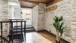 Una escala amb baranes de fusta que condueix a una porta, una paret de pedra i una planta en test.