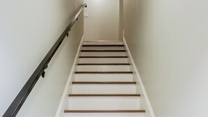 A staircase with wooden steps and a black handrail, leading to a landing with a light fixture. - Stylish Minimalist Stay in City Center (Philadelphia)