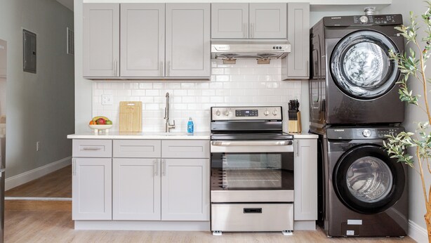 A modern kitchen with grey cabinets, a stainless steel oven, a built-in washing machine, and a tiled backsplash. - Stylish Minimalist Stay in City Center (Philadelphia)