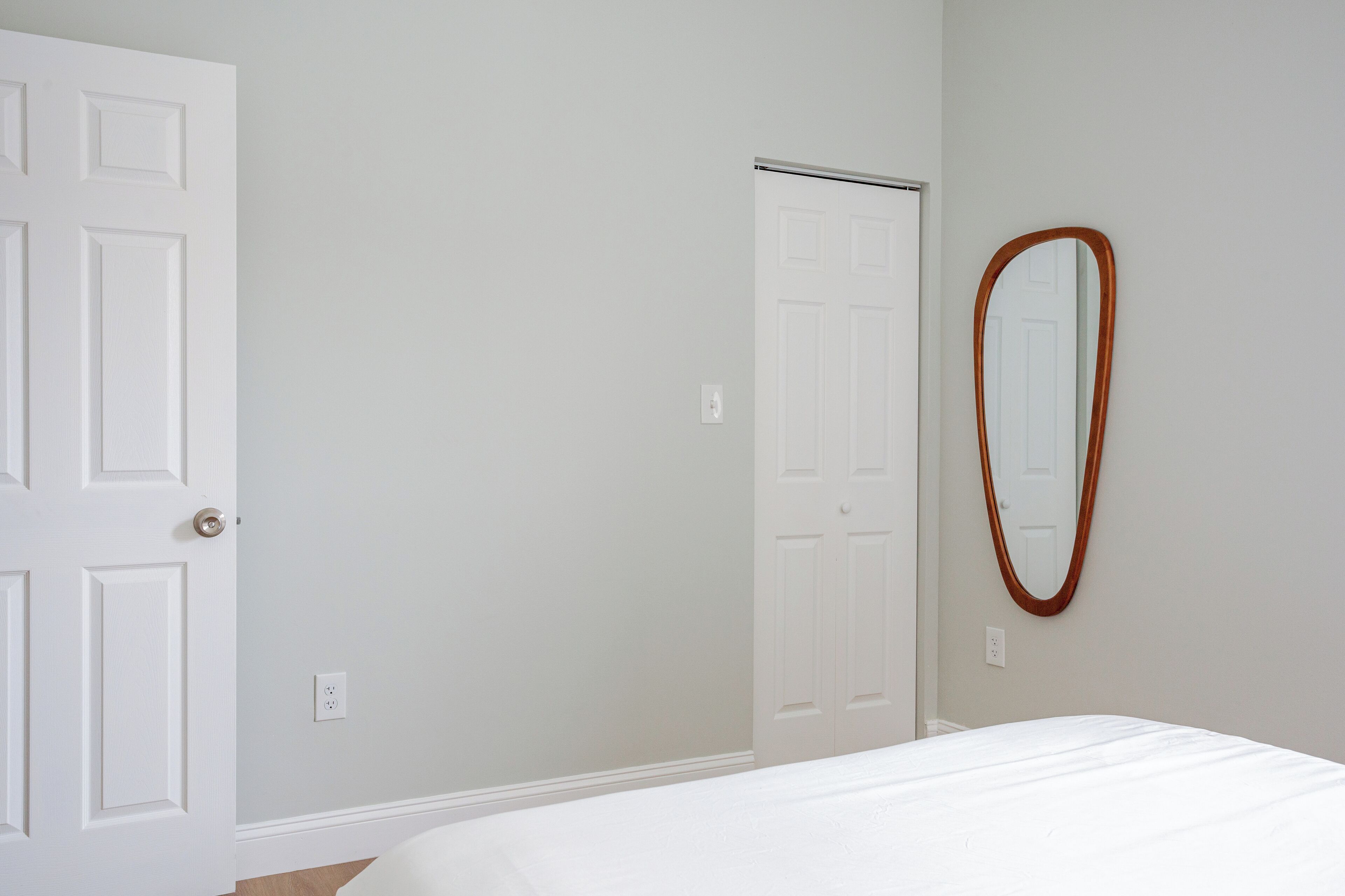 A bedroom with a white door, a white closet, and a mirror on the wall.