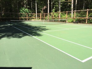 Un court de tennis entouré d’une clôture en bois, avec des arbres en arrière-plan.