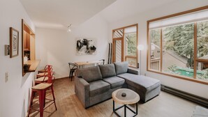Een moderne woonkamer met een grijze modulaire bank, een ronde houten salontafel en een eetgedeelte met rode barstoelen.