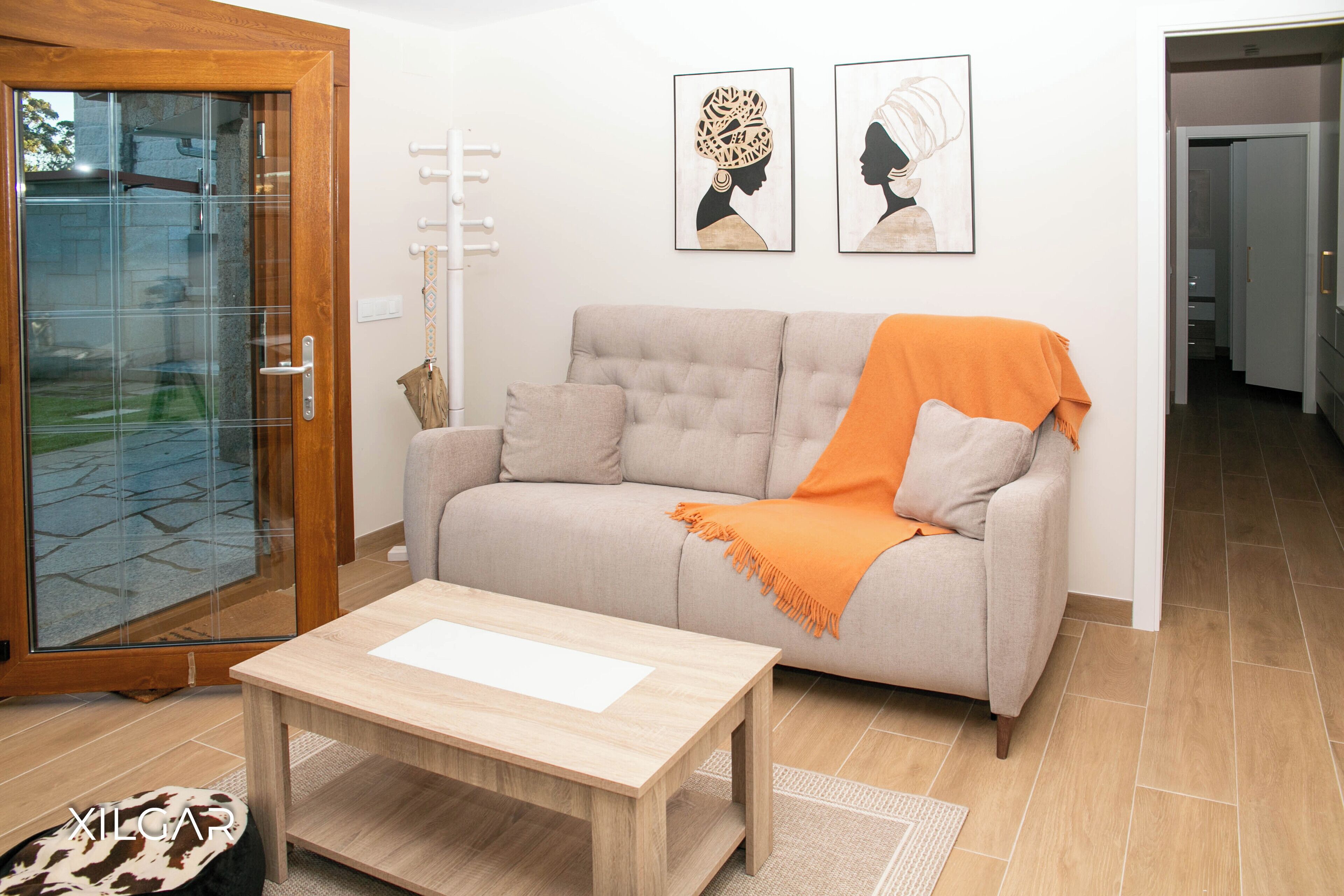 Ein Wohnzimmer mit einem beigen Sofa, einem Holztisch und zwei gerahmten Kunstwerken an der Wand.