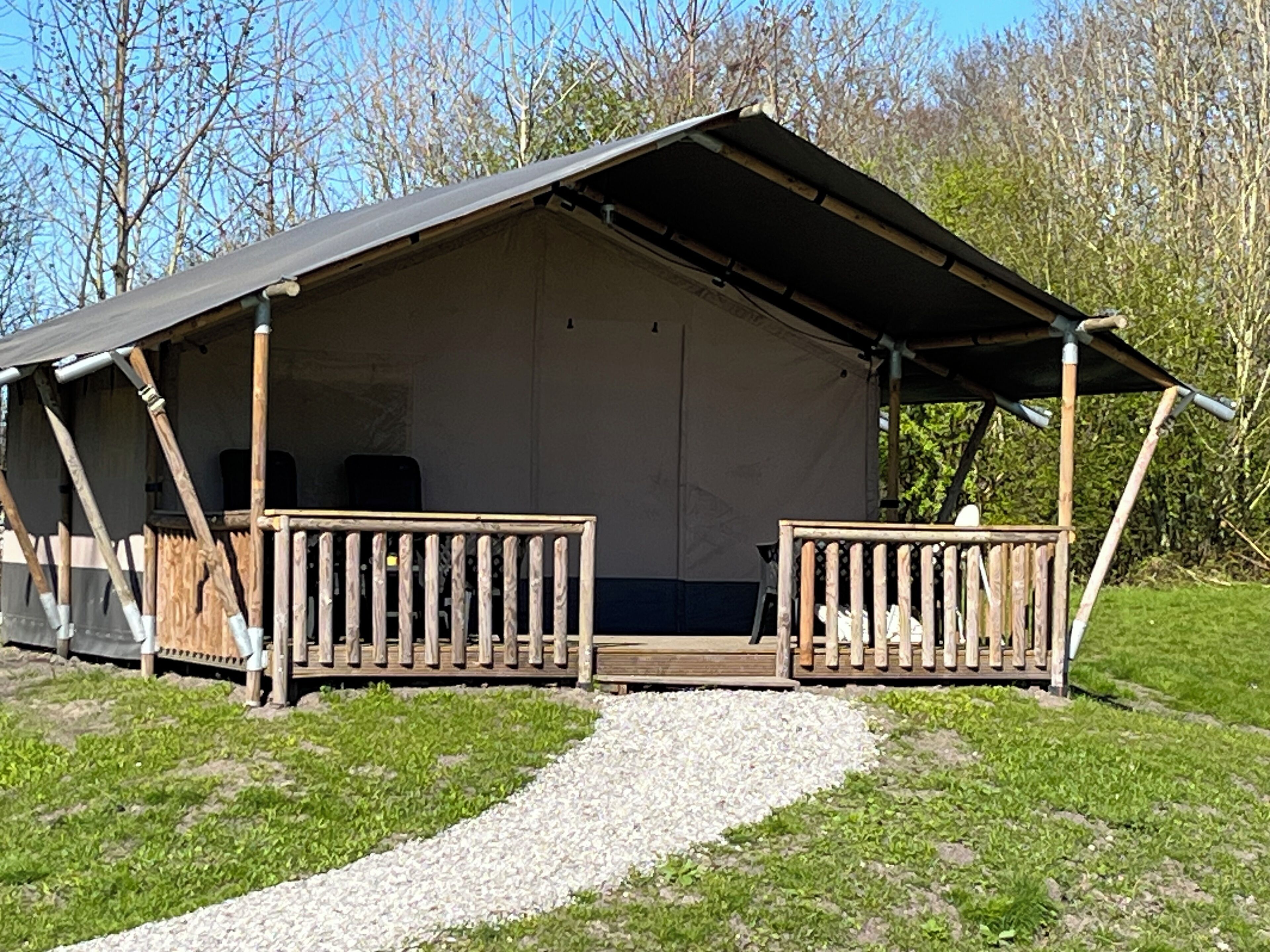 A single-story cabin with a covered porch, a gravel path leading to the entrance, and a natural backdrop of trees.