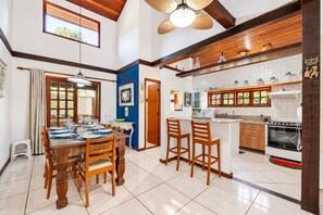 Un comedor con una mesa y sillas de madera, una cocina con muebles blancos y una estufa, y un ventilador de techo.