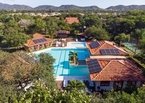 A resort with a swimming pool surrounded by palm trees and solar panels on the roofs. - Bz49 Casa 350m da praia Condomínio (Buzios)