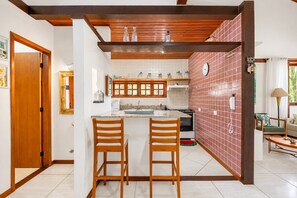 Een keuken met een centraal eiland, houten stoelen, een betegelde achterwand en een houten plafond.
